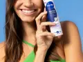 Uśmiechnięta kobieta trzymająca dezodorant Nivea Derma Control na tle niebieskiego tła.