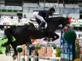 Un cheval noir CSO saute un obstacle coloré, monté par un cavalier en tenue d'équitation.