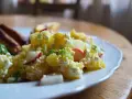 Kartoffelsalat mit Radieschen, Sellerie und Frischkäse auf einem Teller. Daneben liegen Würstchen.