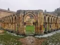 Ruinas de un claustro con arcos de piedra, evocando el nacimiento del Duero. Nieve ligera cubre el césped.