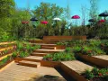 Un jardin aménagé avec des terrasses en bois et une **profondeur marche escalier extérieur** sur plusieurs niveaux, décoré de tulipes rouges et de parasols colorés.