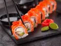 Chopsticks podnoszą kawałek sushi z łososiem i ikrą. Czy sushi jest lekkostrawne? Zależy od składników, ale to wygląda apetycznie.