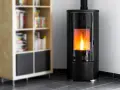 Stufa a pellet moderna in camera da letto, con fiamme vive che illuminano l'ambiente. Accanto, una libreria in legno con libri.