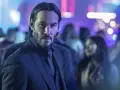 Keanu Reeves w garniturze, w tle rozmyte światła i tłum. Ikona kina akcji, znana z filmów takich jak John Wick.