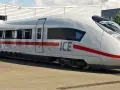 Biały pociąg ICE 5 z czerwonym pasem stoi na torach przed budynkiem.