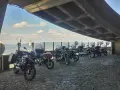 Motocykle pod betonowym zadaszeniem, z widokiem na krajobraz przypominający szwajcarskie Czechy.