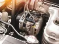 Zbliżenie na alternator samochodowy w komorze silnika, z widocznymi przewodami i elementami mechanicznymi.