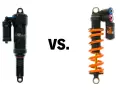 A black air shock and an orange coil shock are shown side-by-side, illustrating the coil vs air shock debate for mountain bikes.