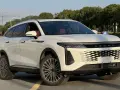Biały OMODA 9 Super Hybrid z czerwonym wnętrzem na tle przemysłowego krajobrazu.