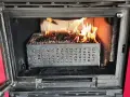 Estufa de pellets ardiendo dentro de un hueco de chimenea. El combustible se quema en una bandeja metálica perforada.