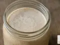 Ein Glas mit aktivem Sauerteig, bereit für die Zubereitung von Brot. Die kahmhefe zeigt sich in feinen Bläschen.