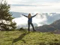 Frau mit ausgebreiteten Armen auf einem Hügel, umgeben von Nebel und Herbstfarben. Das Gefühl von Freiheit und die Bedeutung des Pilgerns werden hier spürbar.