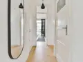 Un ampio specchio nel corridoio riflette le porte bianche e il pavimento in parquet.