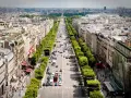 Vista aérea de la **Champs-Élysées** en París, con tráfico y peatones paseando entre los árboles y edificios.