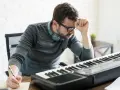 Mężczyzna zamyślony nad klawiaturą, szukający inspiracji, by jego głos prowadzący melodię zabrzmiał idealnie.