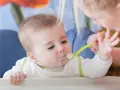 Mama karmi dziecko łyżeczką do karmienia niemowląt. Maluch z zaciekawieniem patrzy na jedzenie.