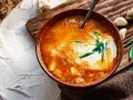 Un tazón de sopa de ajo con crema y cebolleta, acompañado de ajos y cebolletas.