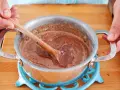 Hände rühren eine schokoladige Masse in einem Topf. So einfach lässt sich die Glasur selber machen für Kuchen oder Gebäck.