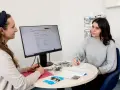 Zwei Frauen besprechen am Tisch eine Webseite zur allgemeinen Studienberatung. Eine Frau schreibt Notizen, die andere schaut auf den Monitor.