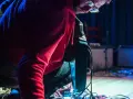 Musiker mit roten Kapuzenpullover beugt sich über ein Pedalboard, um den "Delay"-Effekt einzustellen.