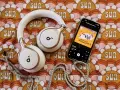 Białe słuchawki i smartfon z okładką audiobooka "Kocie kłopoty grzecznego psa" leżą na kolorowym tle z motywem słońc. Idealne do słuchania książek z lektorem.