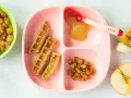 Baby-freundliche Apfelwaffeln mit Apfelmus und Zimt-Apfelstückchen auf einem rosa Teller. Ein halber Apfel und eine Banane liegen daneben.