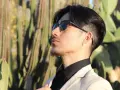 Uomo con abito beige e camicia nera, occhiali da sole, tra i cactus. Un look elegante per ogni occasione.