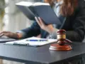 Sądowy młotek i dokumenty na biurku. Prawnik w tle studiuje akta, zastanawiając się, czy radca prawny może być obrońcą.