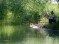 Dwaj wędkarze siedzą nad zieloną wodą, czekając na branie. Jeden z nich, starszy mężczyzna, skupiony na swoim sprzęcie, gotowy do **casting spinning**.