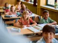 Dzieci w klasie skupione na lekcji. Uczennica pisze w zeszycie, obok niej leży piórnik. To pokazuje, co na koncentrację u dzieci: nauka i zaangażowanie.