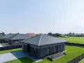 Nowoczesne domy z szarym dachem z blachodachówki, otoczone zielonymi trawnikami i ogrodzeniami.