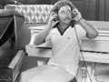 Billy Powell hört mit Kopfhörern Musik, während er neben einem Klavier sitzt.