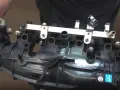 Hands hold a black plastic intake manifold with a fuel rail and sensors. This part is crucial for intake manifold runner control.