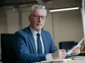 Poważny mężczyzna w garniturze analizuje dokumenty, zastanawiając się, ile komornik może zabrać z 13 pensji.