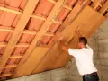 Operaio installa pannelli per la coibentazione del tetto in legno, migliorando l'isolamento termico.