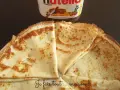 Crêpes dorées prêtes à être garnies, avec un pot de Nutella en arrière-plan. Une recette facile pour des crêpes maison !