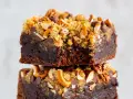 Zwei gestapelte, saftige fudge brownies, garniert mit Brezelstückchen, Nüssen und Schokostückchen.