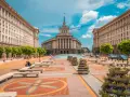 Słoneczna pogoda w Bułgarii w lipcu. Sofia, plac przed budynkiem Narodowego Zgromadzenia, z drzewami i kwiatami.