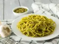 Pyszny makaron z pesto, podany na białym talerzu, obok czosnku i miseczki z sosem.