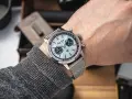 Mężczyzna prezentuje swój lśniący zegarek Breitling, gotowy do czyszczenia. Metalowa bransoleta i tarcza z chronografem błyszczą.