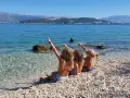 Trzy dziewczynki siedzą na kamienistej plaży w Chorwacji, wskazując palcami na morze. Idealne miejsce, gdzie do Chorwacji z dziećmi.