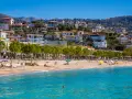 Albania, pogoda czerwiec: słoneczny dzień na plaży, turkusowe morze, piaszczysty brzeg, zielone drzewa i białe budynki na wzgórzu.