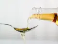 Apfelessig wird aus einer Flasche auf einen Löffel gegossen. Ein Tropfen für das Abnehmen.