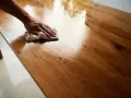 Mano che lucida un tavolo di legno con un panno, mostrando come ravvivare il legno vecchio con un trattamento che ne esalta la venatura.