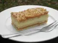 Szybkie ciasto z masą krówkową i budyniem, z orzechami na wierzchu, na białym talerzu z widelcem.