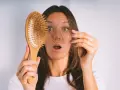 Frau mit erschrockenem Gesicht hält Haarbürste mit Haaren. Hoffnung auf progesteron haare wachsen wieder.