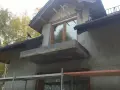 Niedokończona elewacja domu z balkonem i oknem. Na dachu siedzi ptak.
