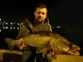 Wędkarz trzyma dużą rybę, złowioną nocą. To dowód, że skuteczne przynęty na sandacza działają nawet w ciemności.