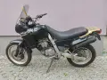Czarny motocykl Aprilia Pegaso 650 z złotym bagażnikiem i lusterkami, zaparkowany na kostce brukowej.