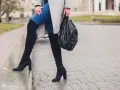 Kobieta w kozakach na obcasie i jeansach, trzymająca plecak. Aby buty się nie ślizgały, warto zastosować specjalne nakładki.